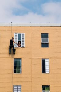 man hanging on building near woman in window during daytime